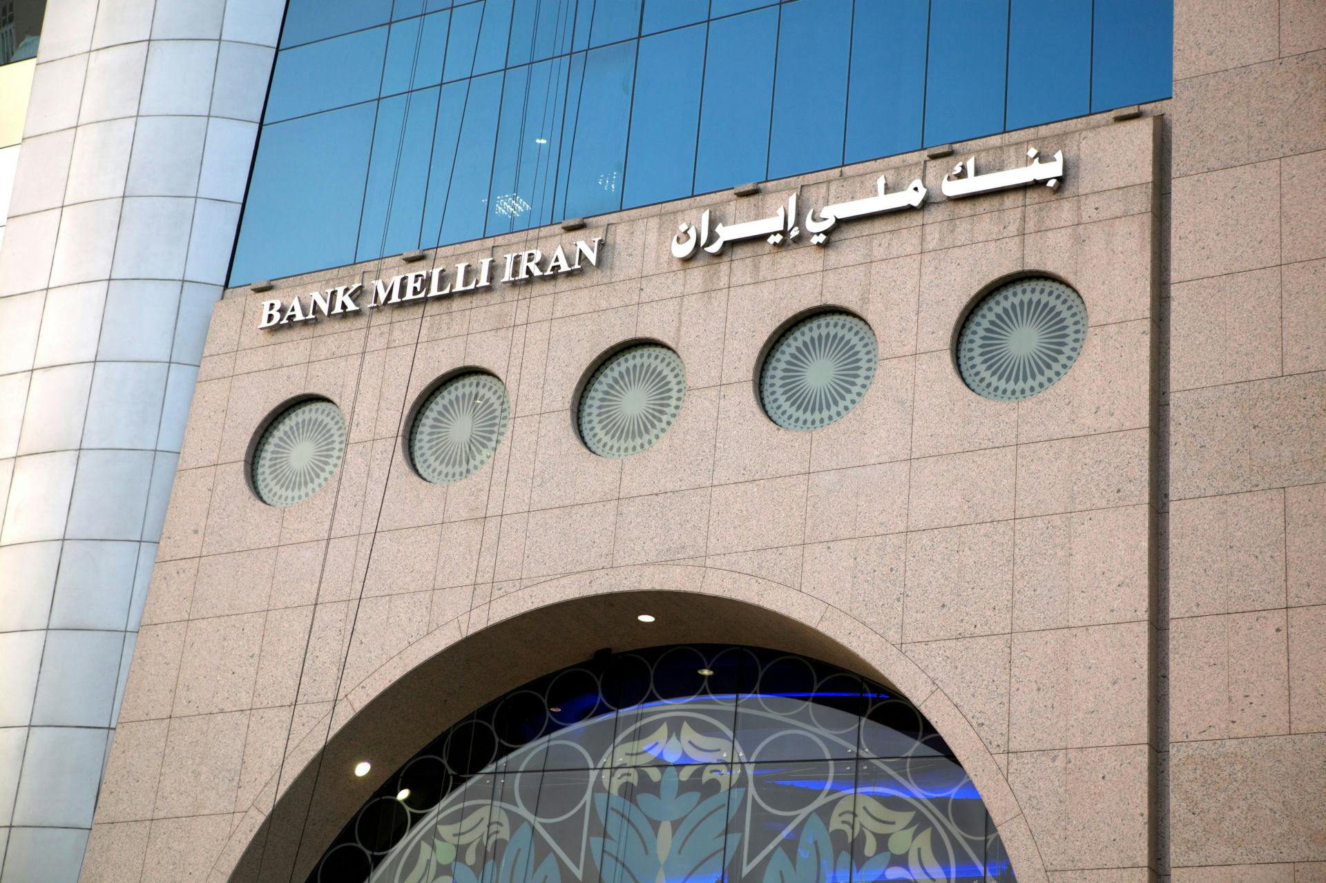 The outside of the Bank Melli Iran building features the name of the bank in Farsi letters on one side and in English for international audiences on the other above a soaring arch reminiscent of a Middle Eastern mosque.